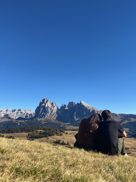 Noelia y Pablo sentados frente a las montañas del Alpe di Siusi